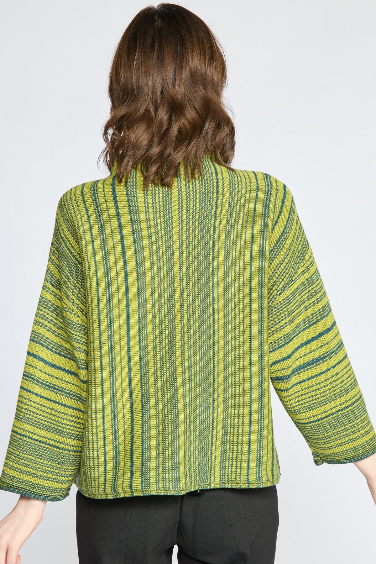 A woman viewed from the back wearing a cropped, wide-sleeved striped top in lime green and dark green, paired with black pants, against a light gray studio background.