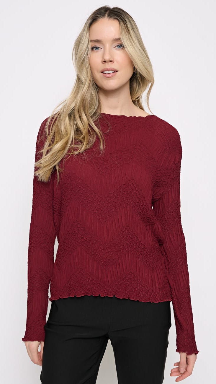 A woman modeling a textured, long-sleeve knit sweater in deep burgundy with a scalloped neckline, paired with black pants, against a plain white studio background.