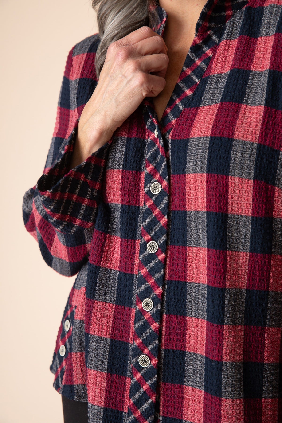Close-up of a person wearing a red and blue plaid shirt against a beige background
