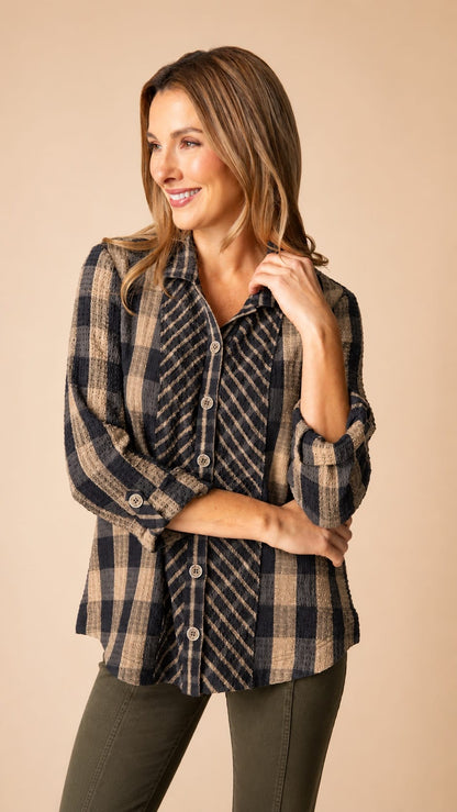 A woman modeling a long-sleeve button-up plaid shirt in navy and beige, paired with dark olive pants, against a solid beige studio background.
