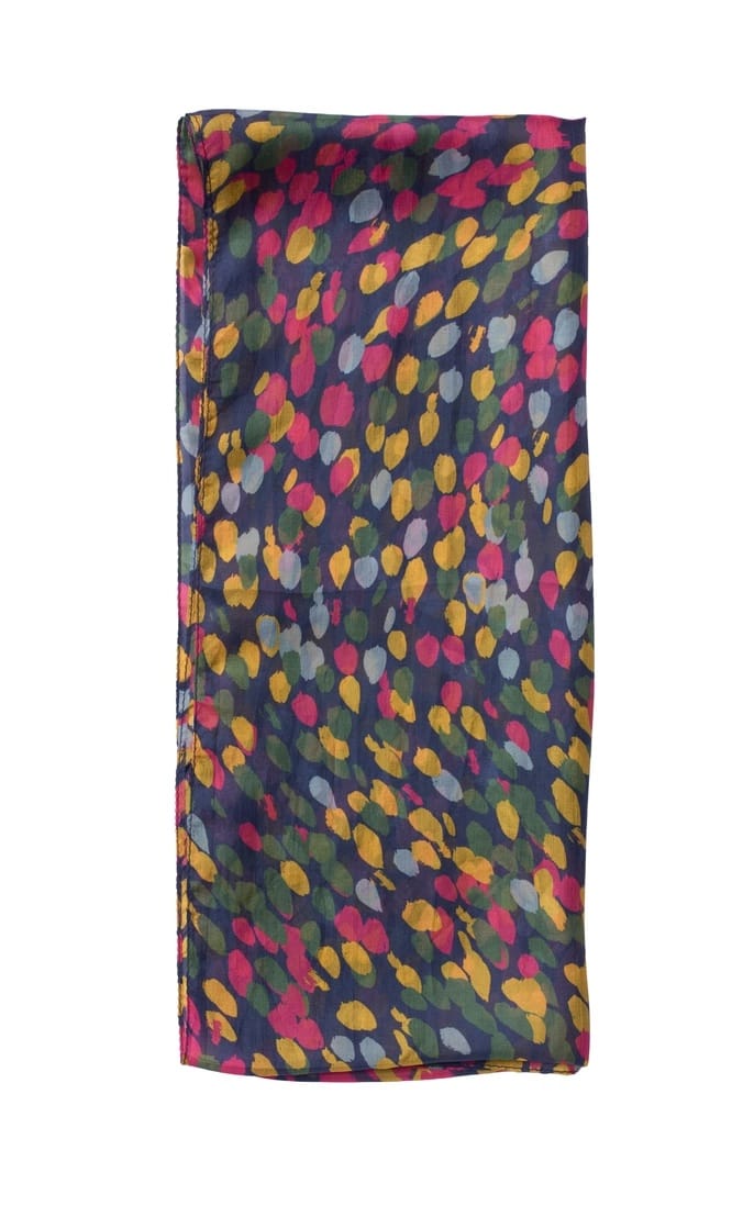 A folded silk scarf featuring a colorful abstract leaf or droplet pattern in pink, yellow, green, and gray on a dark navy blue background, set against a plain white studio backdrop.