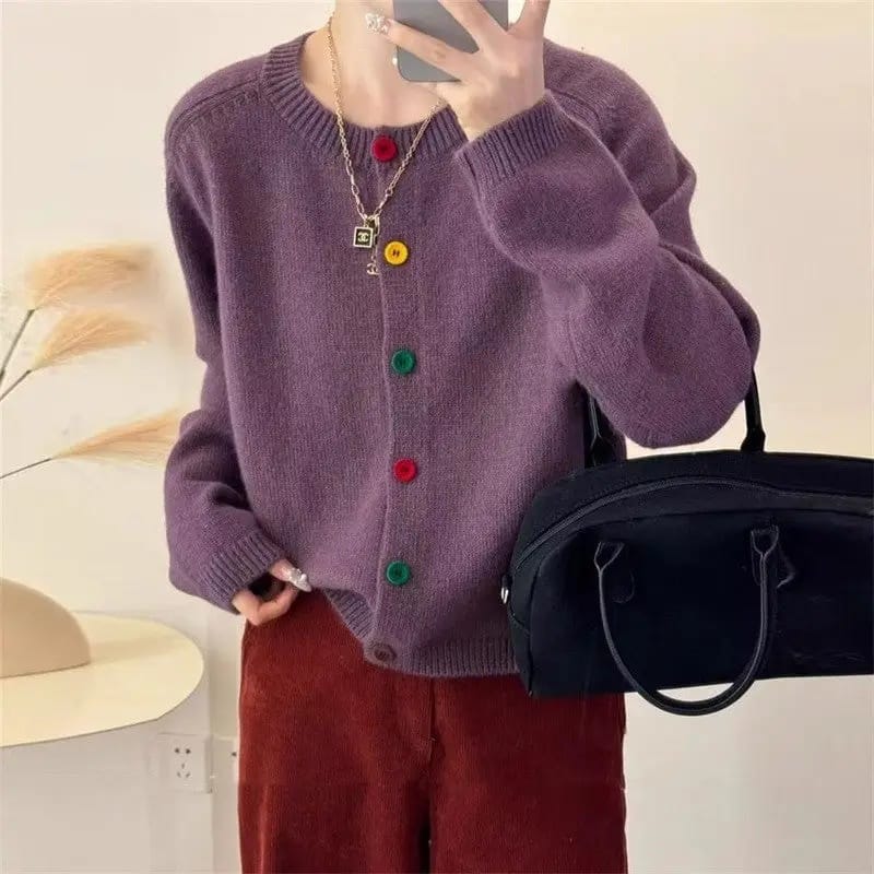 Person wearing a purple cardigan with colorful buttons, holding a black bag, and taking a selfie.