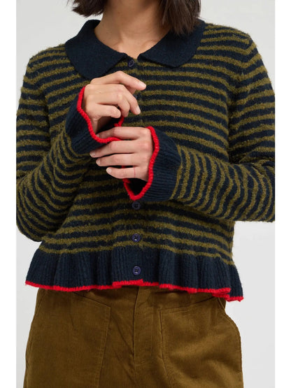 A person wearing a striped knit cardigan with a dark navy collar, cuffs, and hem, accented with bright red trim, paired with brown corduroy pants against a light gray studio background.