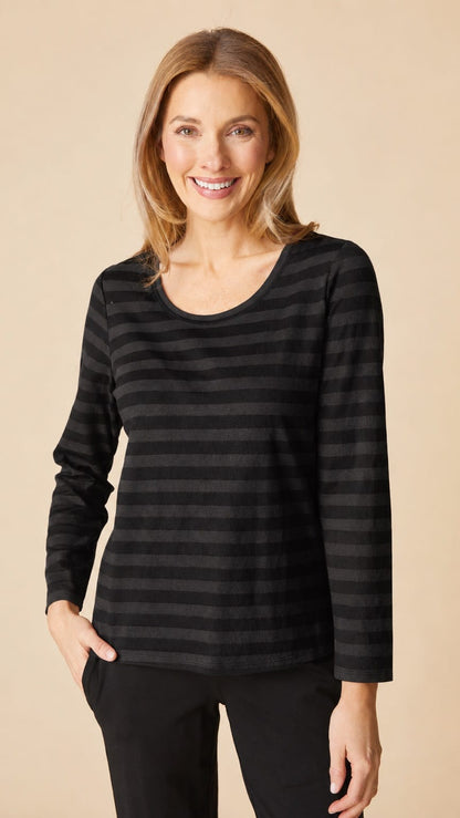 A woman wearing a black long-sleeve scoop-neck top with horizontal dark gray stripes, paired with black pants, standing against a solid beige background.