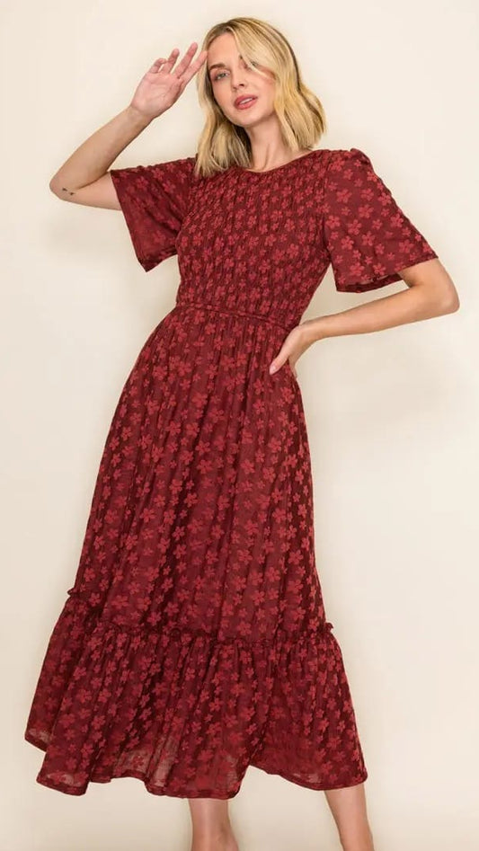 A woman modeling a red midi dress with a floral pattern, short puff sleeves, and a tiered skirt against a plain beige background.