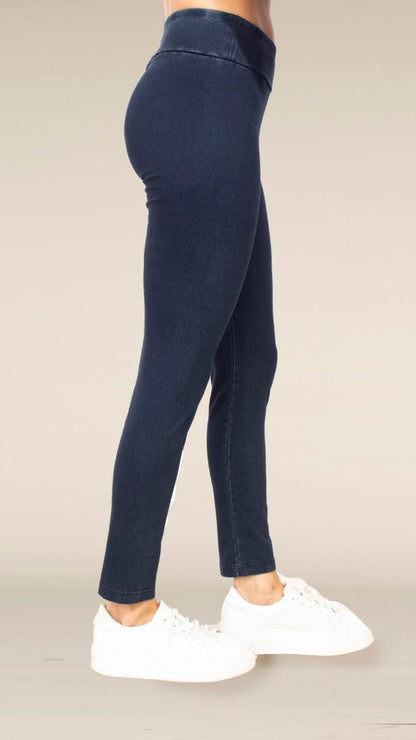 A person shown from the waist down wearing dark navy blue skinny leggings and white platform sneakers against a plain beige studio background.