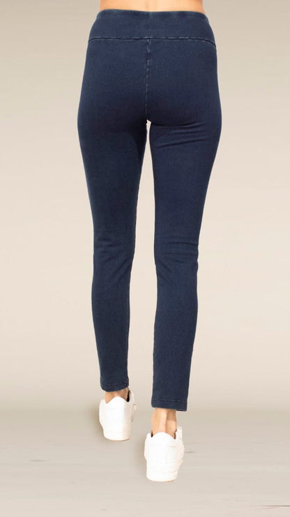 Rear view of a person wearing dark navy blue skinny jeans and white sneakers against a plain light beige studio background.