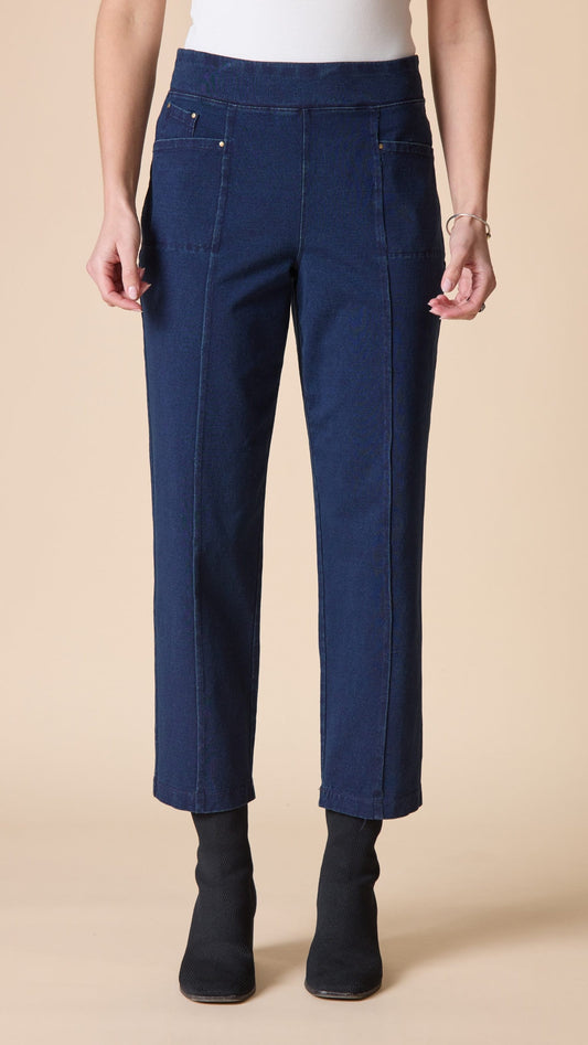 A model wearing dark blue cropped jeans with front patch pockets, paired with black ankle boots, shown from the waist down against a solid beige background.