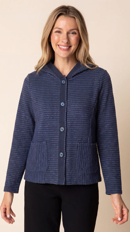 A woman wearing a navy blue hooded cardigan with thin white vertical stripes, front buttons, and two front patch pockets, paired with black pants, against a solid beige background.