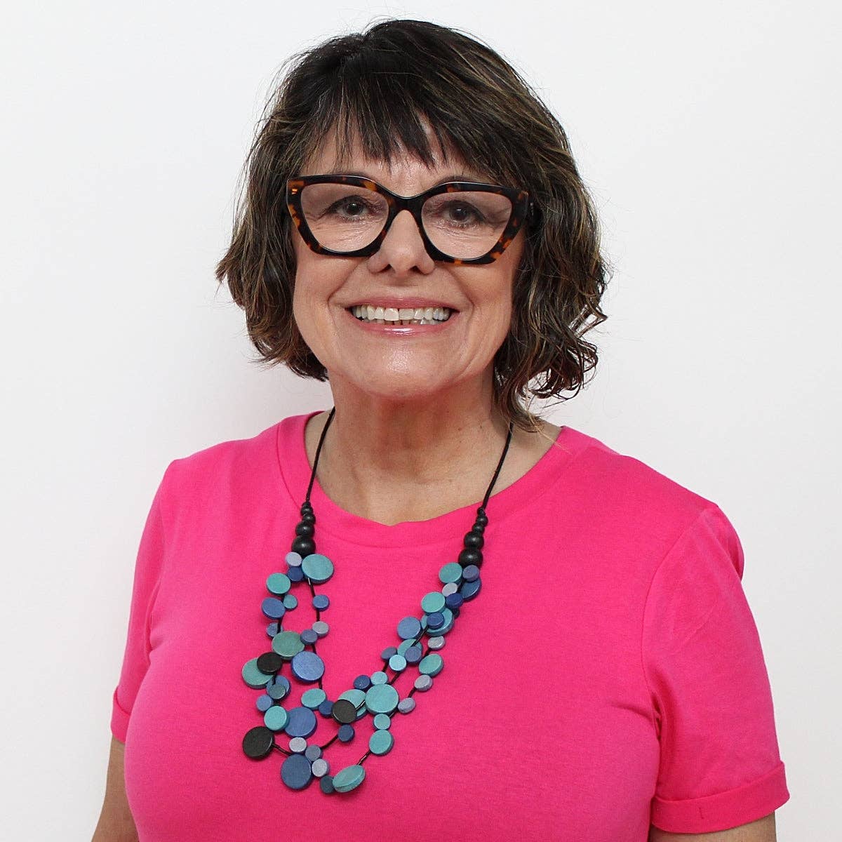 Woman wearing a pink shirt and colorful necklace against a white background