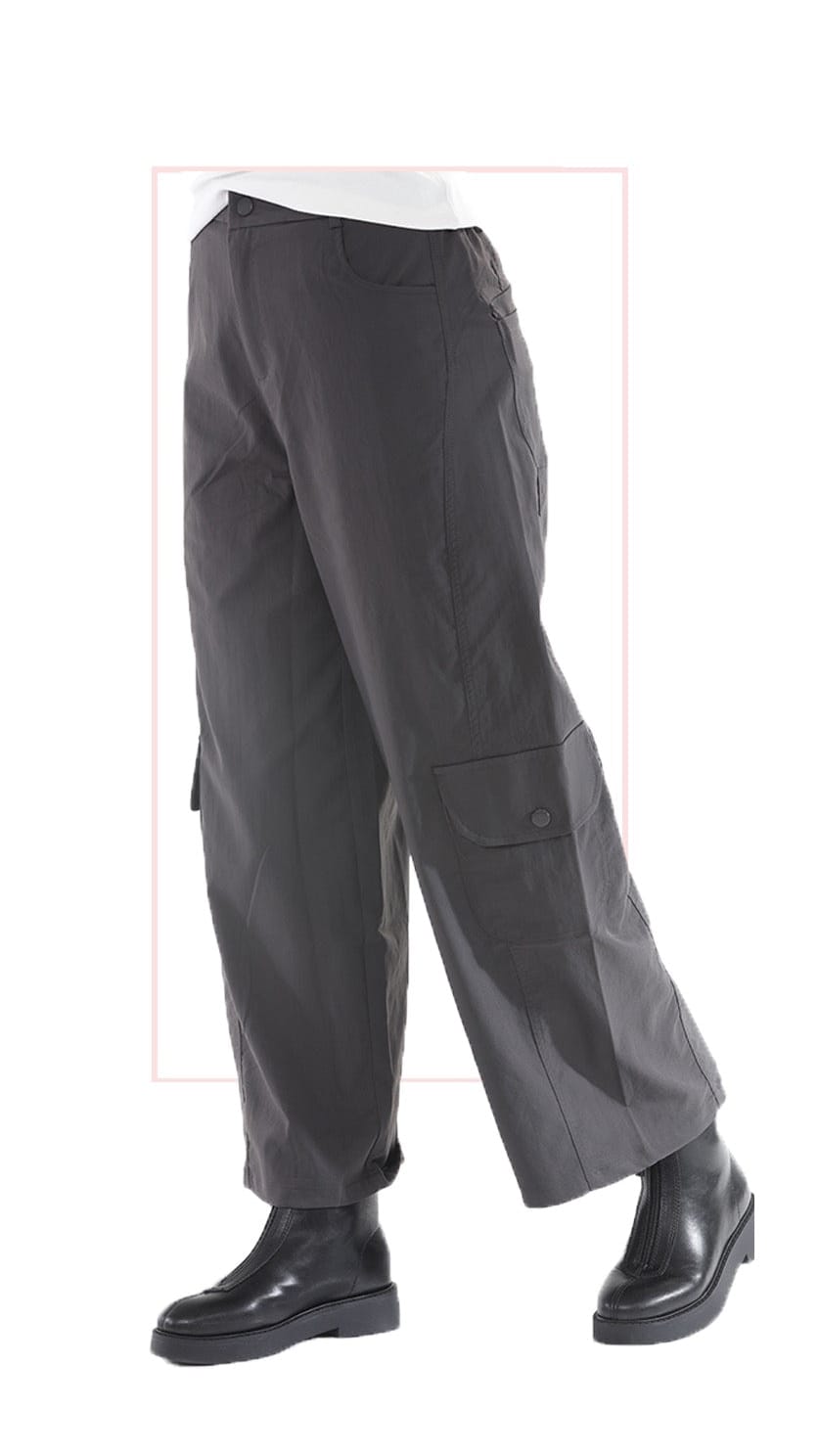 A pair of dark gray wide-leg cargo pants with flap pockets, shown on a model from the waist down wearing black boots against a white background.