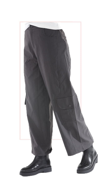 A pair of dark gray wide-leg cargo pants with flap pockets, shown on a model from the waist down wearing black boots against a white background.