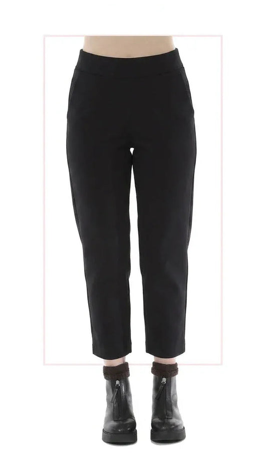 Black narrow pants shown on a lower-body mannequin or model form, paired with black ankle boots, against a white background with a faint pink rectangular outline.