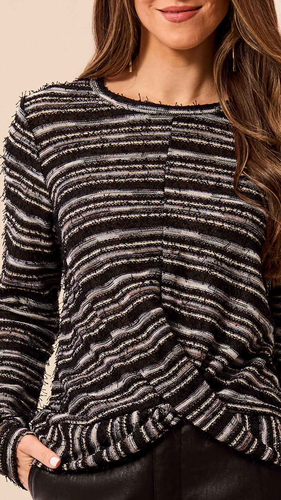 A close-up of a woman wearing a black and gray textured knit sweater with horizontal stripes and a twisted front detail, paired with black pants.
