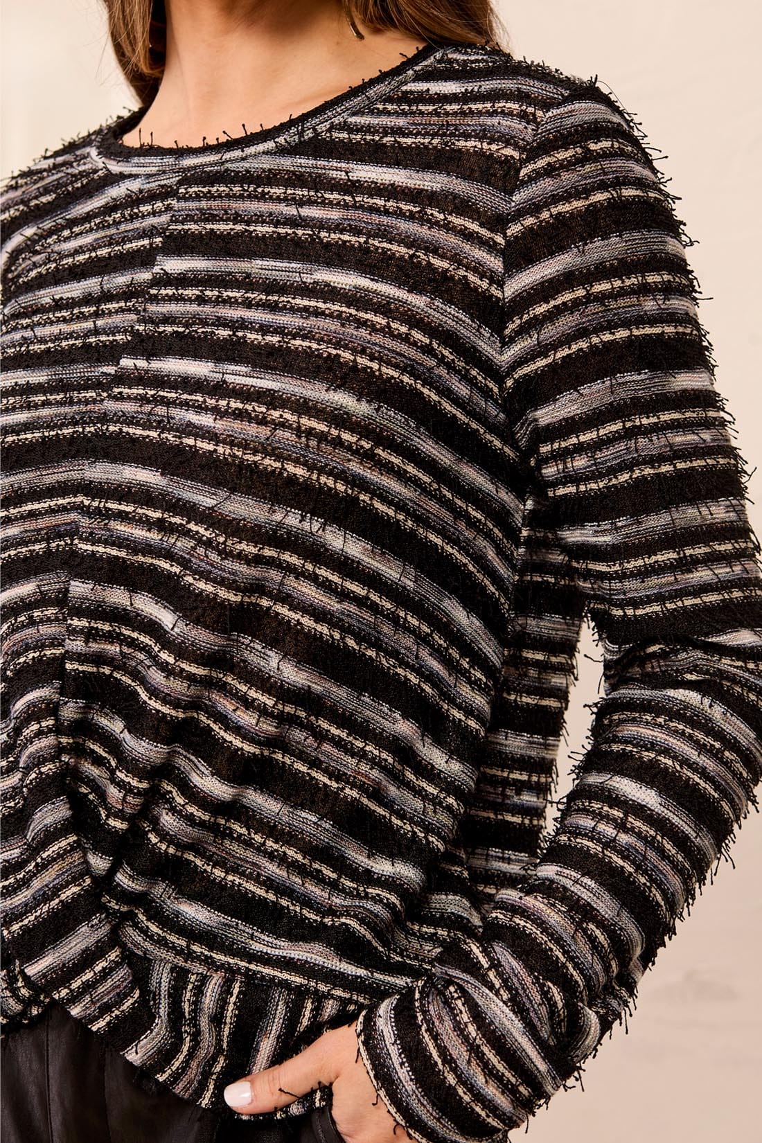 A close-up of a person wearing a long-sleeve knit top with horizontal black, gray, and white textured stripes and frayed edges.