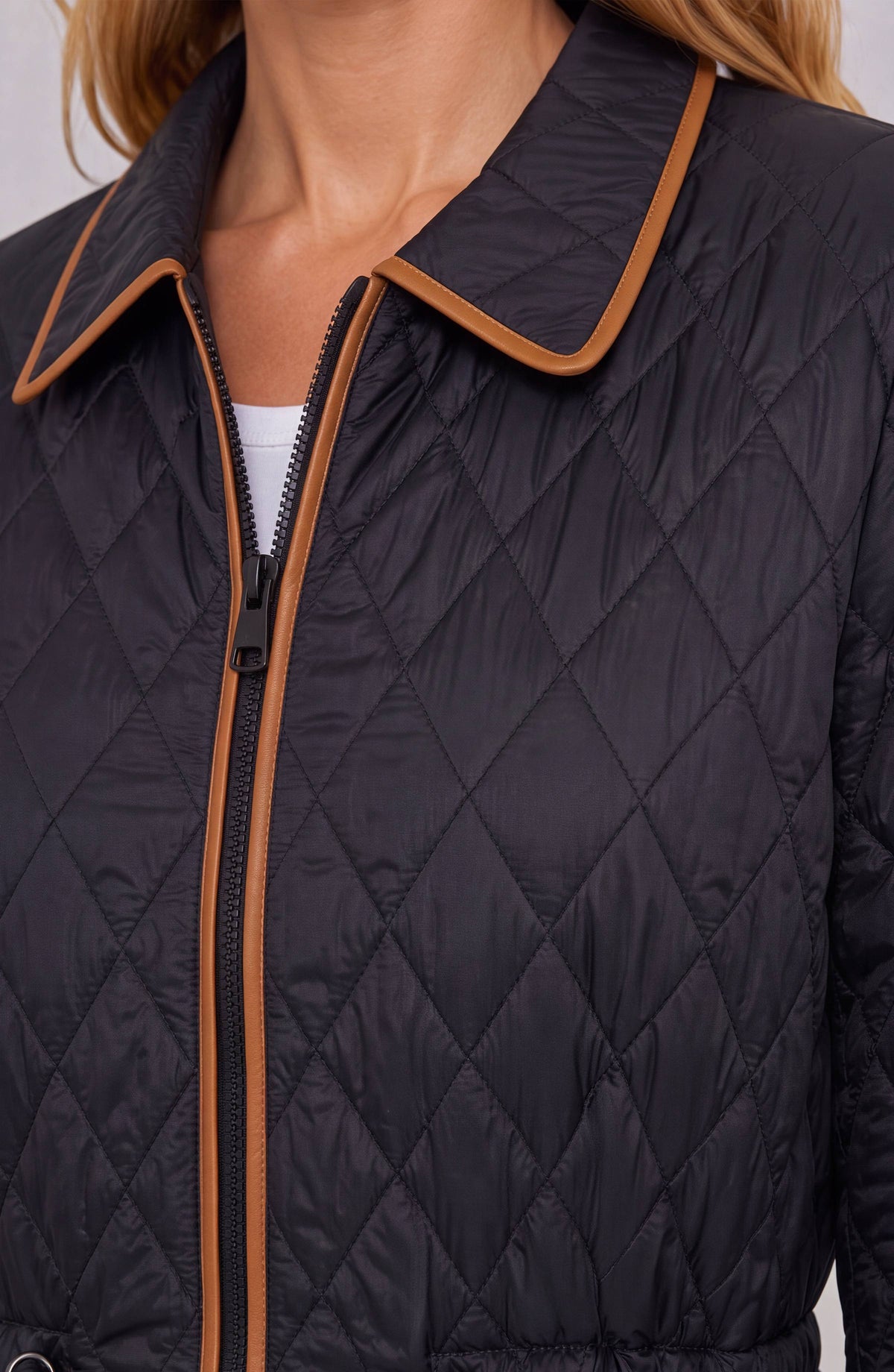 Close-up of a quilted jacket with diamond stitching, featuring a dark navy body and contrasting tan trim along the collar, zipper, and front opening.