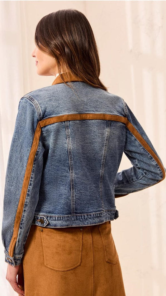 A woman shown from the back wearing a cropped blue denim jacket with contrasting brown suede-like shoulder and side panels, paired with a brown skirt, against a soft cream background.